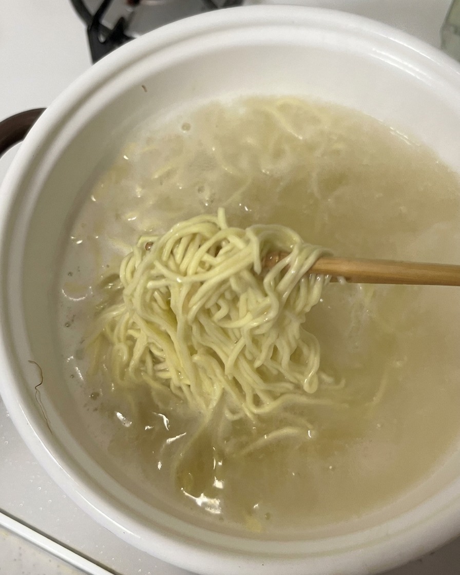 젓가락으로 냄비에서 삶은 면을 건져 올리는 모습.