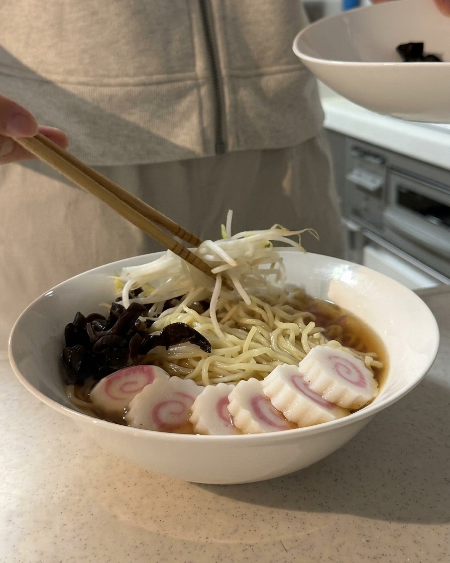 목이버섯과 어묵이 올라간 라멘 위에 데친 숙주나물을 젓가락으로 올리는 모습.