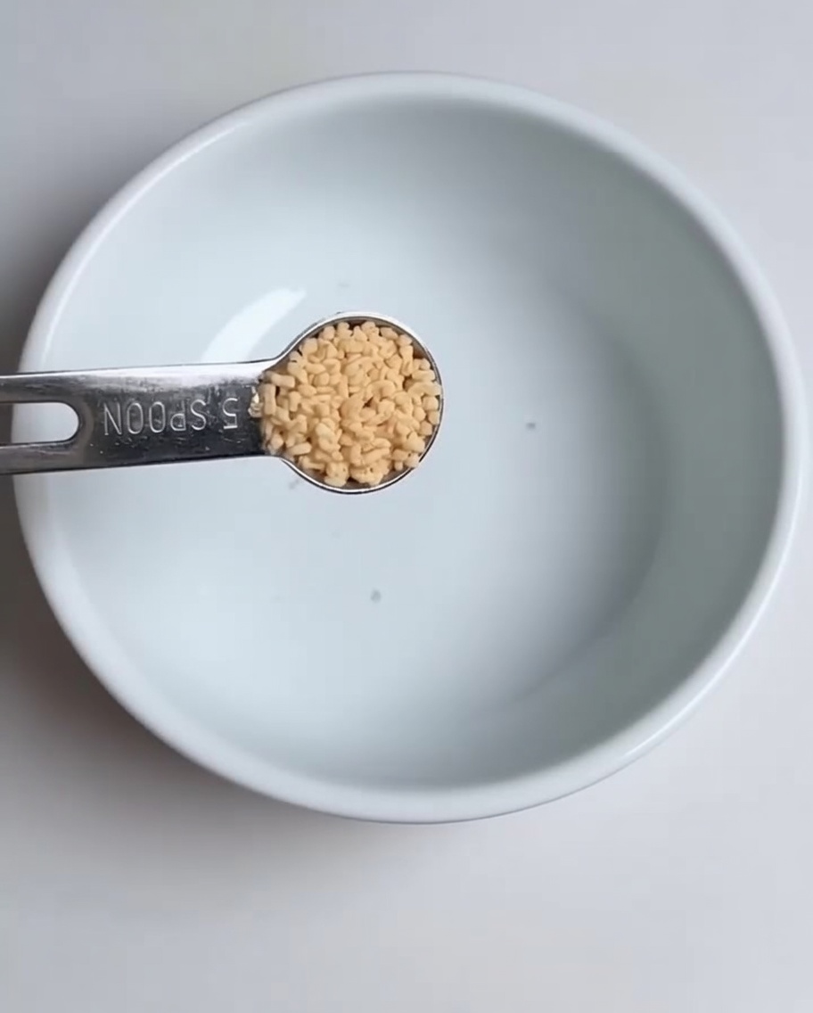 흰 그릇에 계량 스푼으로 닭고기 육수 분말을 넣는 근접 사진.
