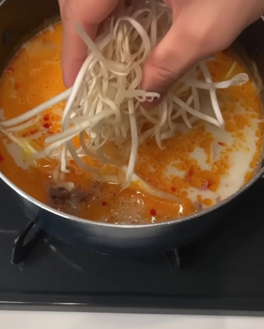 크리미한 국물 요리에 손으로 숙주나물을 한 줌 넣는 모습.