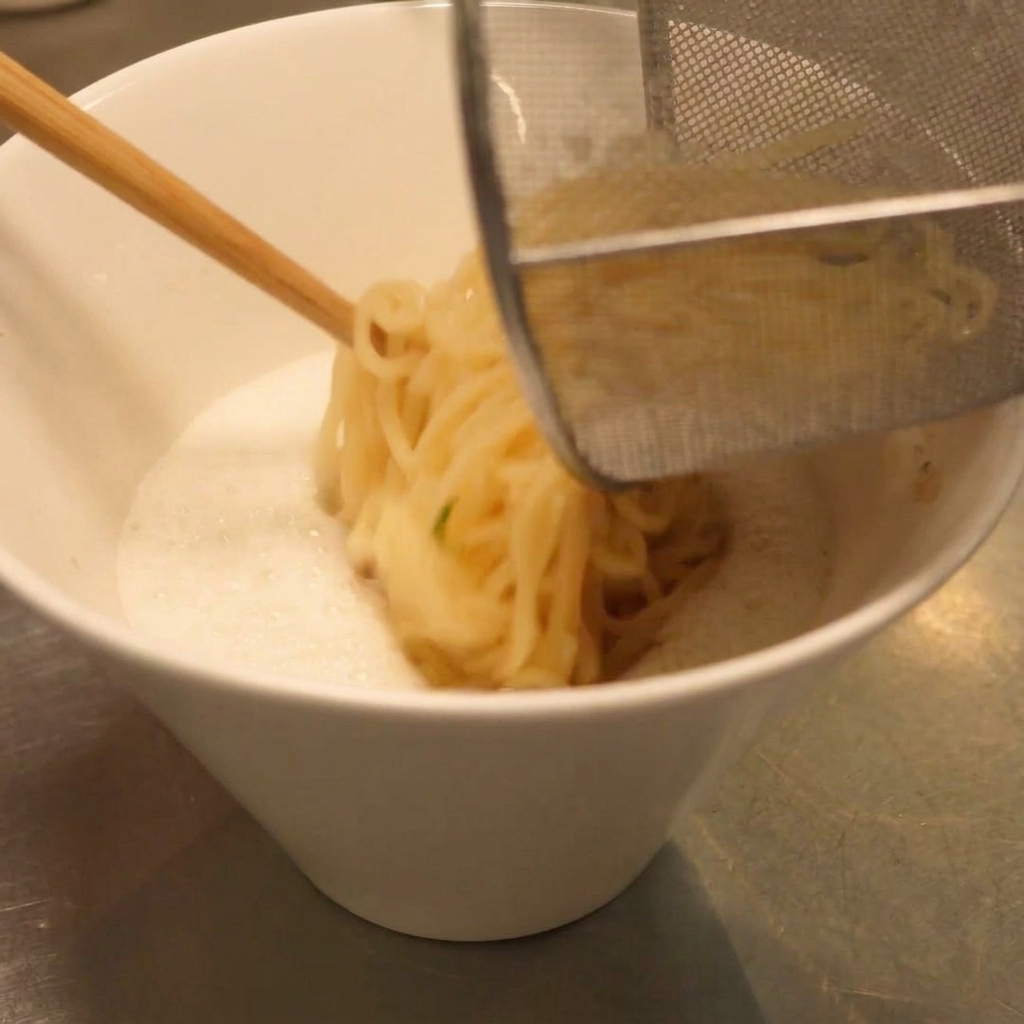 물기를 뺀 라멘 면을 크리미한 육수 그릇으로 옮기는 모습.