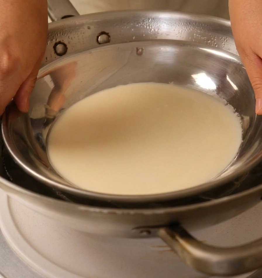 끓는 물 위의 찜기에 반죽이 담긴 금속 접시를 올리는 모습.
