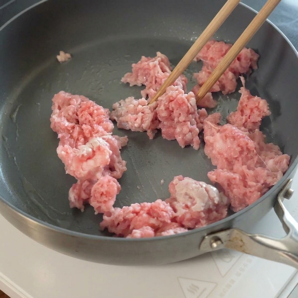 볶은 돼지고기에 슬라이스한 마늘을 넣는 모습.