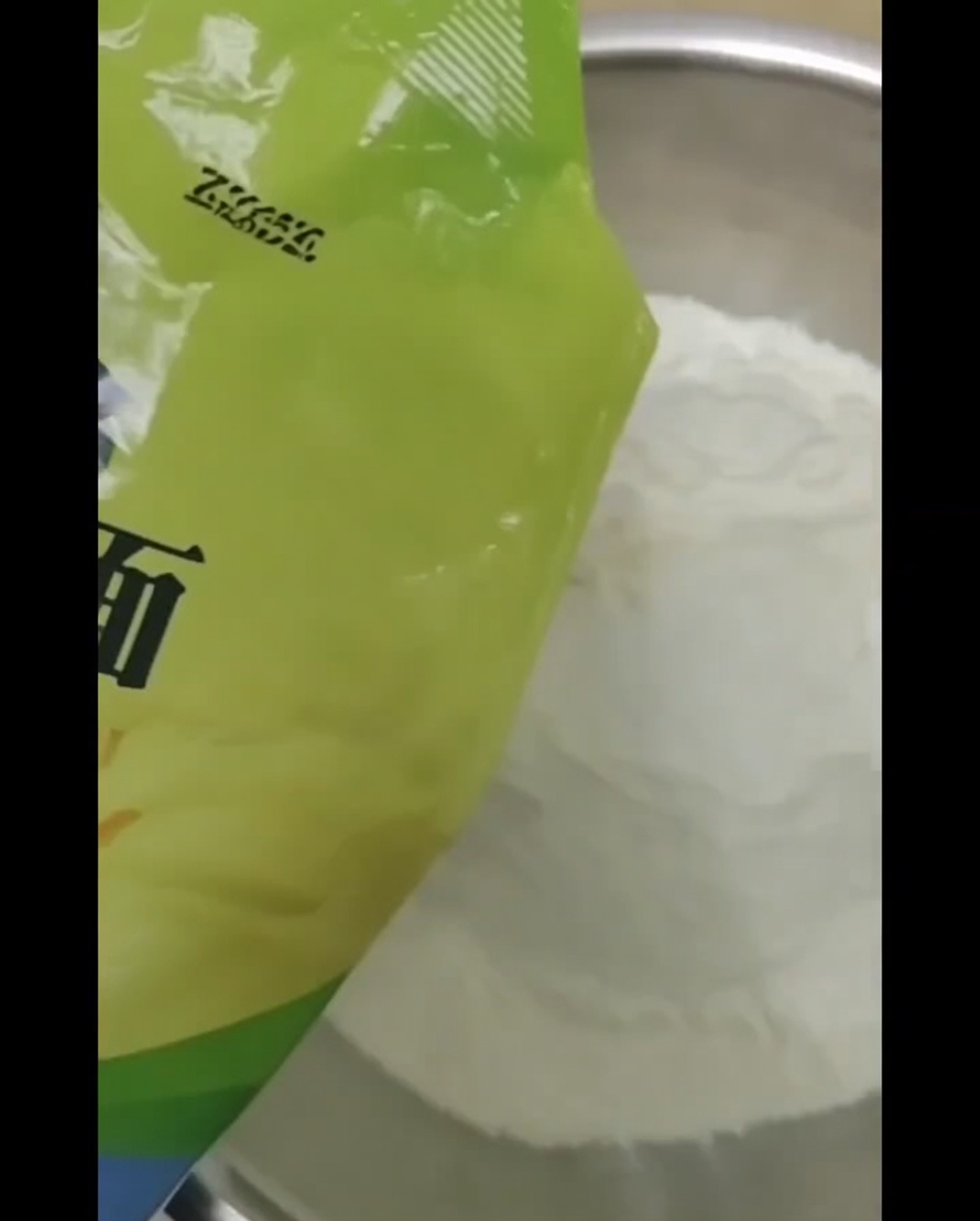 밀가루가 담긴 큰 볼에 물을 붓고 숟가락으로 섞는 근접 사진.