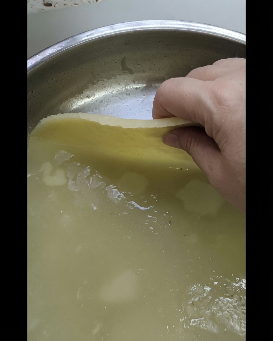 손으로 넓게 펴진 반죽을 반짝이는 금속 트레이 위에 올리는 모습.