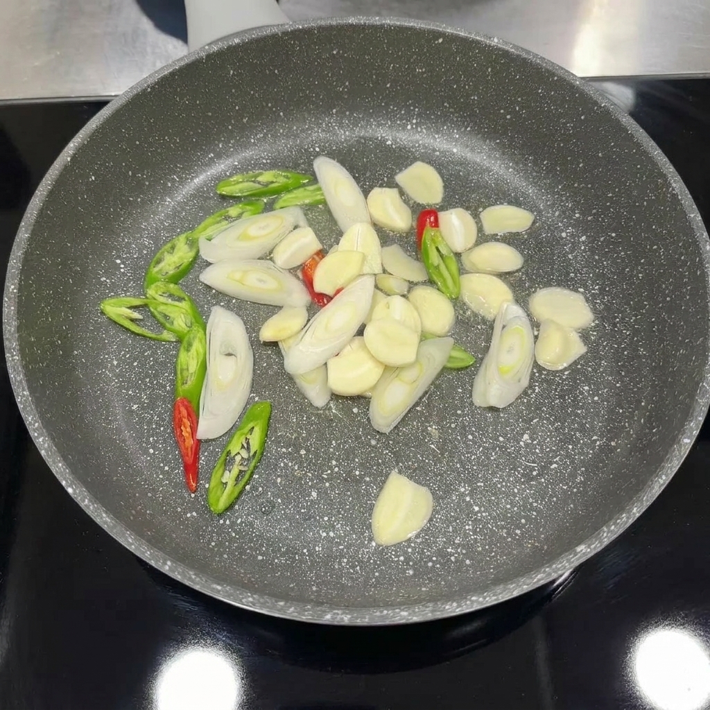 팬에서 마늘, 고추, 대파를 넣어 향을 내며 볶는 모습.