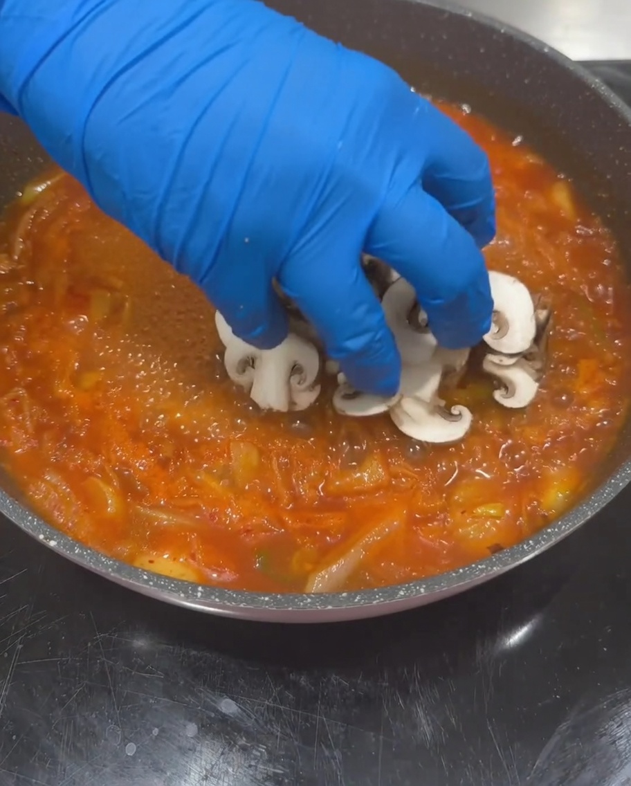끓고 있는 김치 국물에 버섯, 애호박, 두부를 넣는 모습.