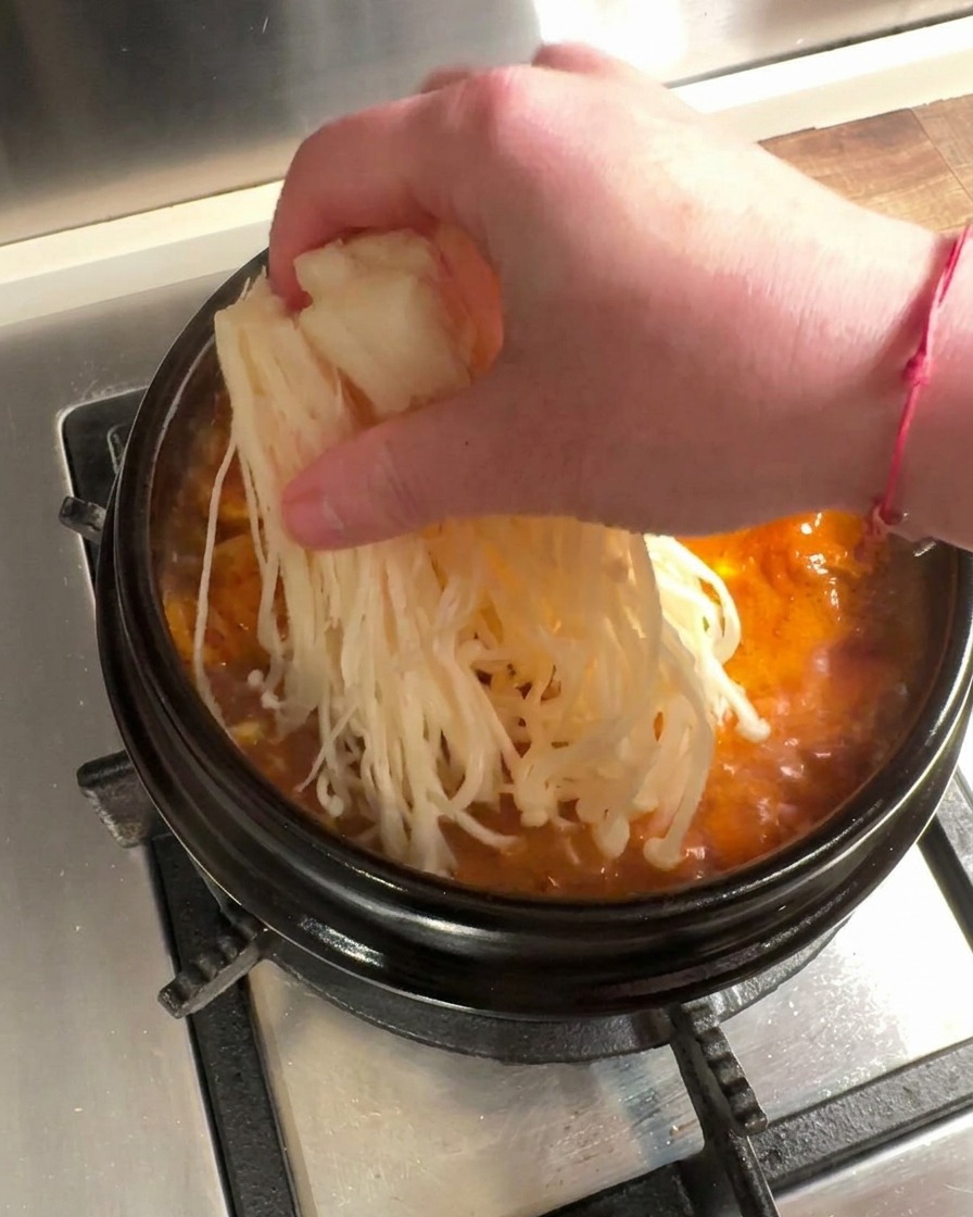끓는 찌개에 소고기와 팽이버섯을 넣는 모습.