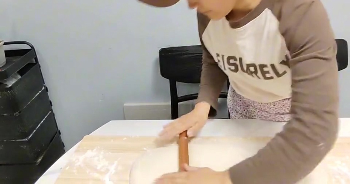 나무 도마 위에서 밀대로 반죽을 얇게 펴는 모습.