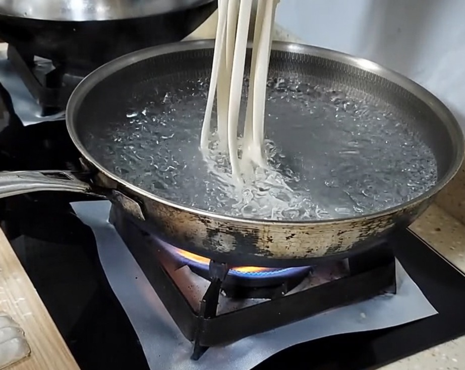 반죽 가닥을 양손으로 늘려 끓는 물에 넣는 모습.