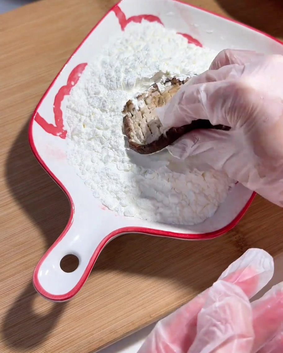 비닐장갑을 낀 손으로 표고버섯의 안쪽면에 옥수수 전분을 묻히는 모습.