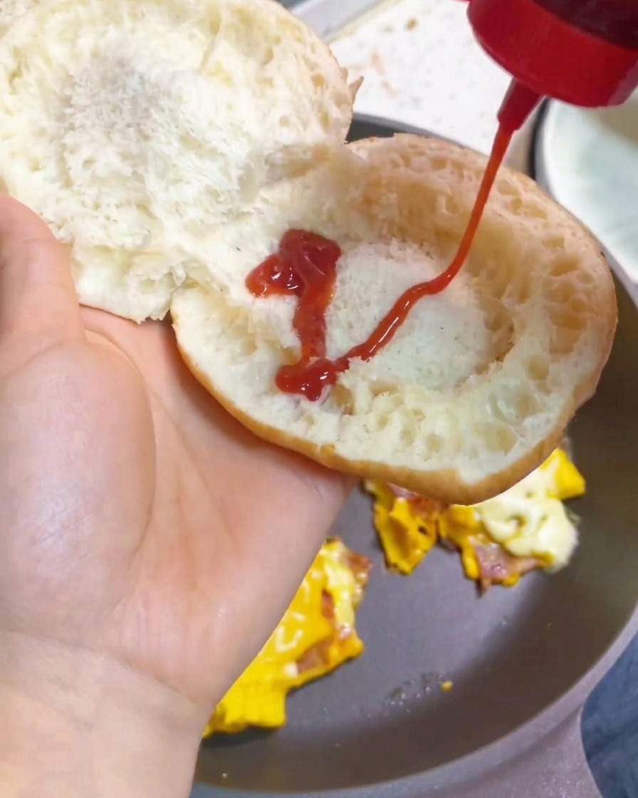 구운 버거 번 안쪽에 토마토 케첩을 지그재그로 뿌리는 모습.