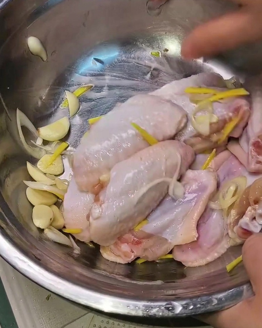 손으로 금속 볼 안의 닭날개와 향신료를 골고루 섞는 모습.