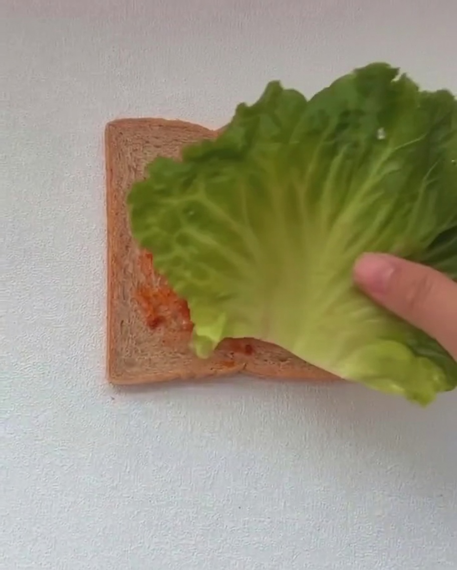 소스가 발린 식빵 위에 싱싱한 상추 두 잎을 올리는 모습.