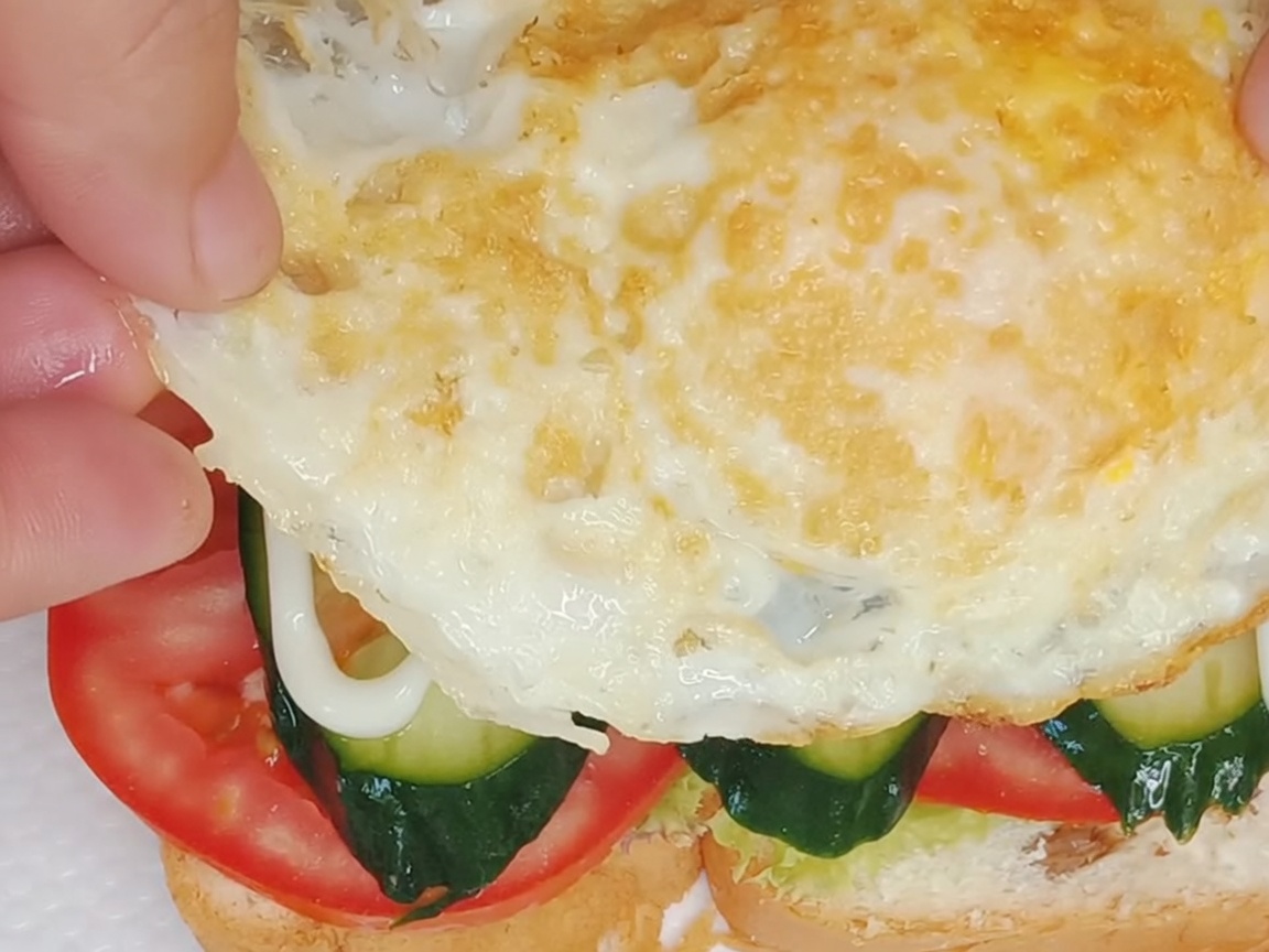조립된 샌드위치 위에 달걀프라이를 얹는 모습.