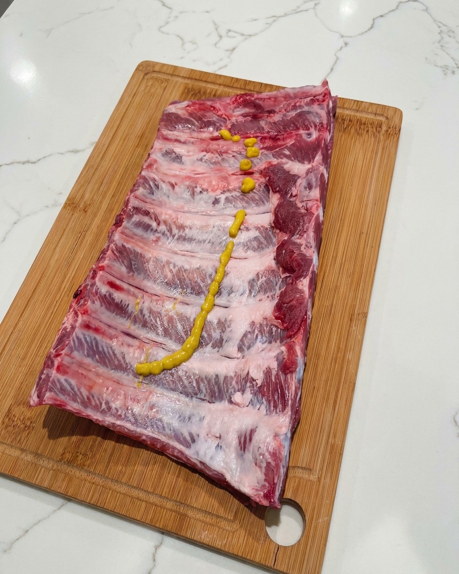 도마 위 폭립 위에 옐로우 머스타드를 길게 짜놓은 모습.