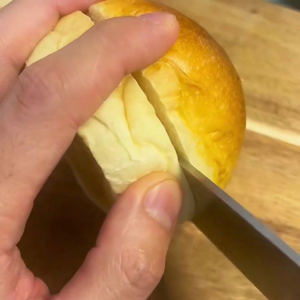 나무 도마 위에서 버거 번을 칼로 반으로 자르는 모습.
