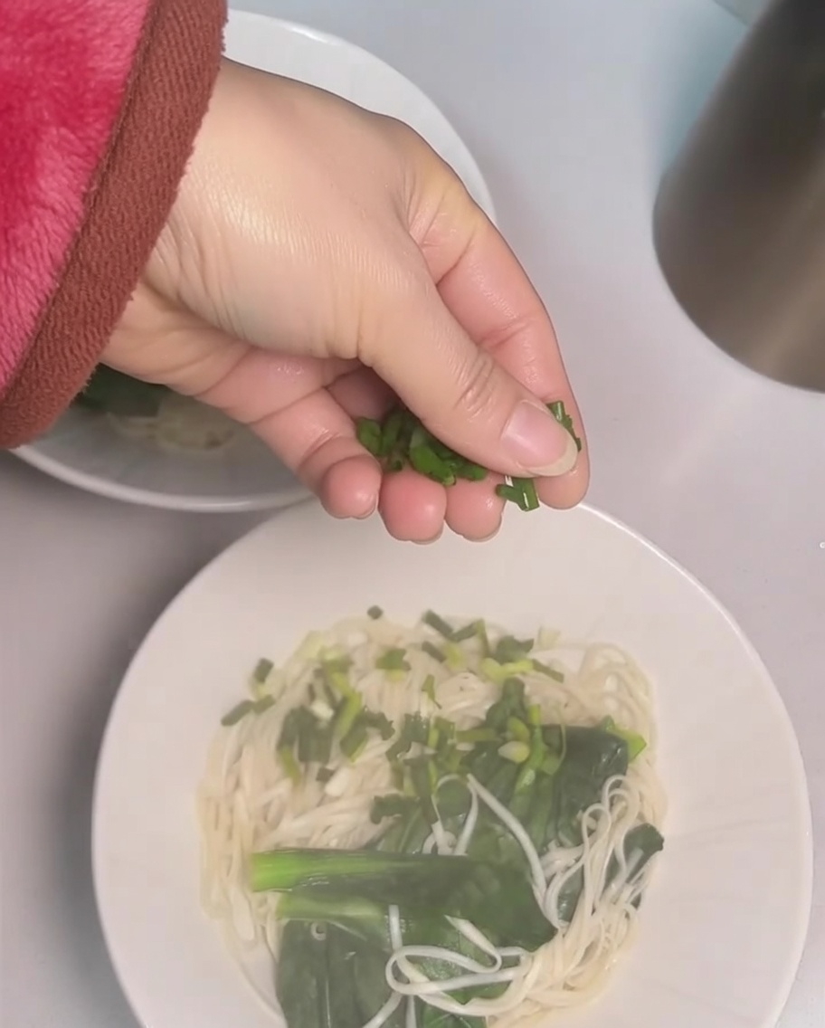 국수 위에 다진 대파를 뿌리는 손.