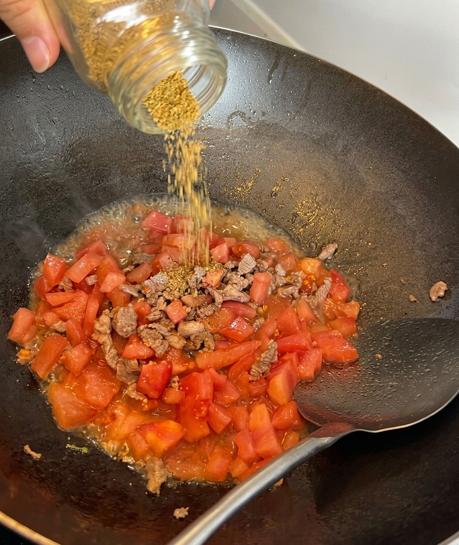 소고기와 토마토가 볶아지고 있는 팬 위에 천일염을 뿌리는 모습.