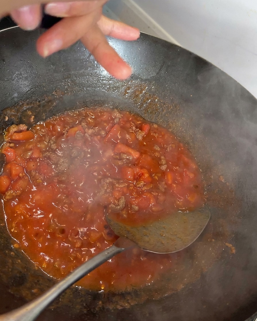 끓고 있는 붉은 토마토 소고기 소스 위에 후추를 갈아 넣는 모습.