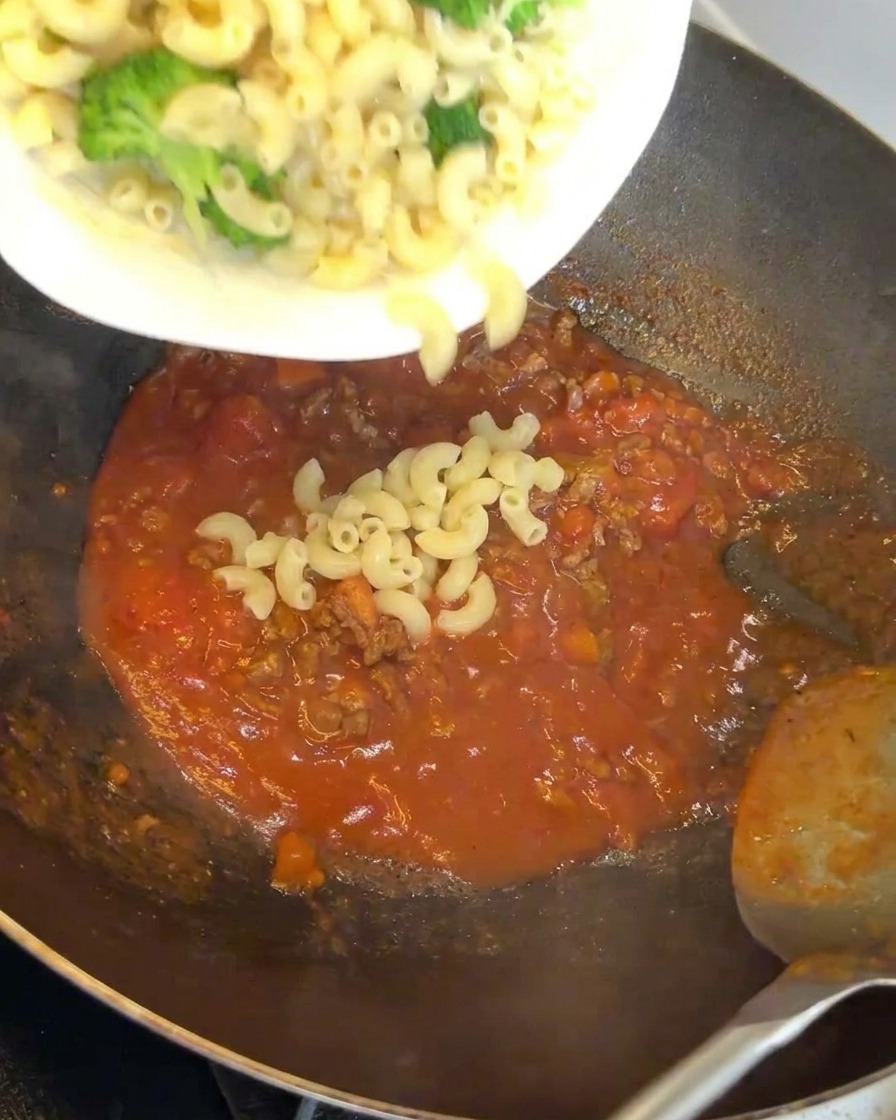 진한 고기 소스가 담긴 웍에 마카로니와 브로콜리를 넣는 모습.