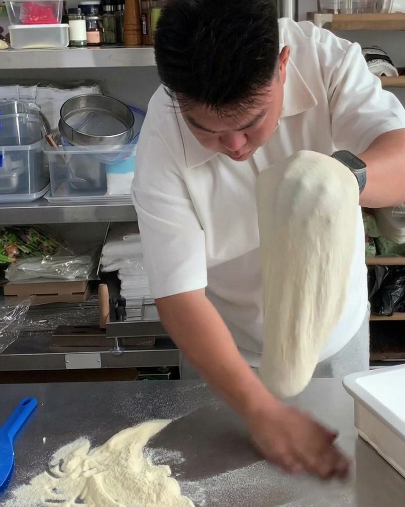 늘려진 도우를 양손으로 번갈아 가며 가볍게 털어 여분의 밀가루를 제거하는 모습.