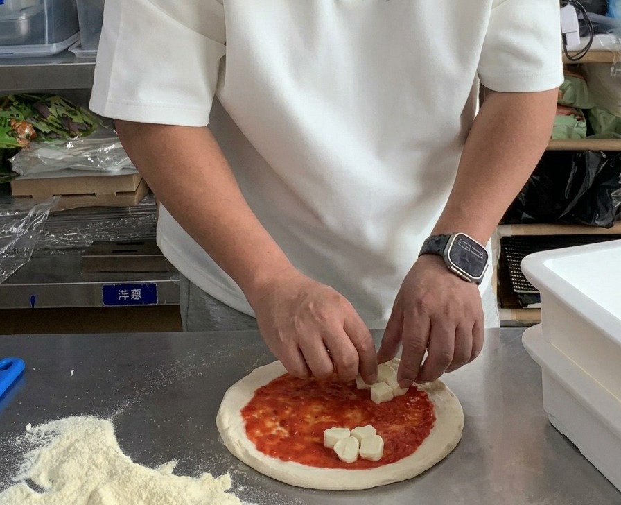 토마토 소스를 바른 도우 위에 깍둑썰기한 모짜렐라 치즈를 올리는 모습.
