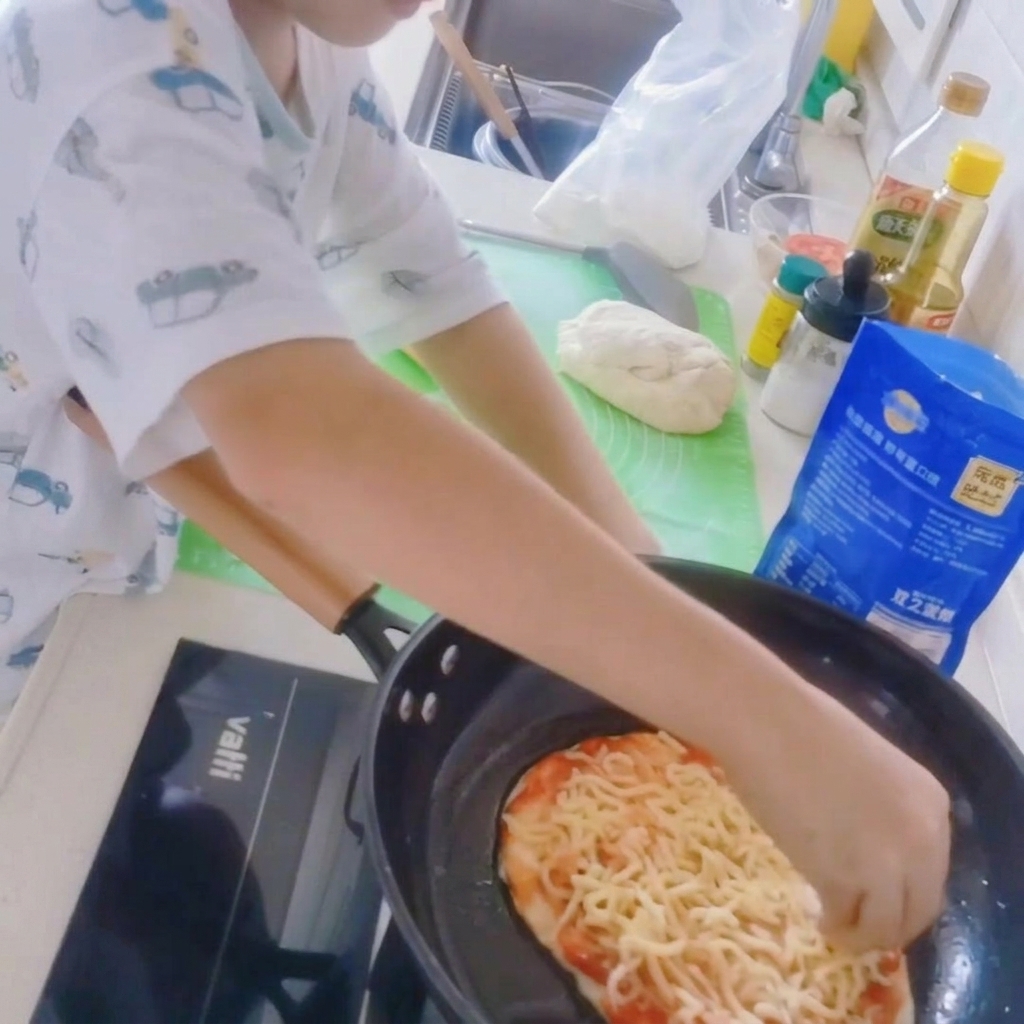 프라이팬 위의 피자 베이스에 슈레드 모짜렐라 치즈를 듬뿍 올리는 모습.
