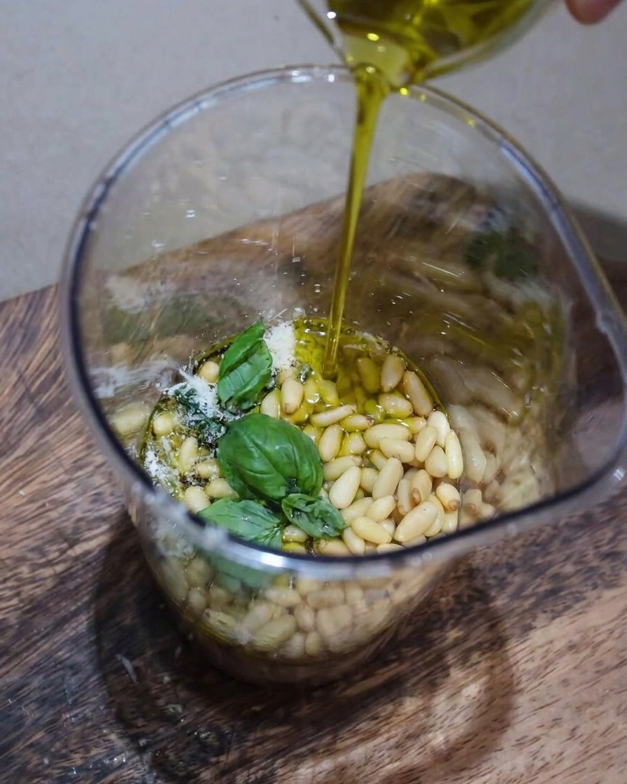 생바질, 잣, 파르메산 치즈 등 페스토 재료가 블렌더 안에서 갈리며 올리브 오일이 가늘게 떨어지는 클로즈업 모습.