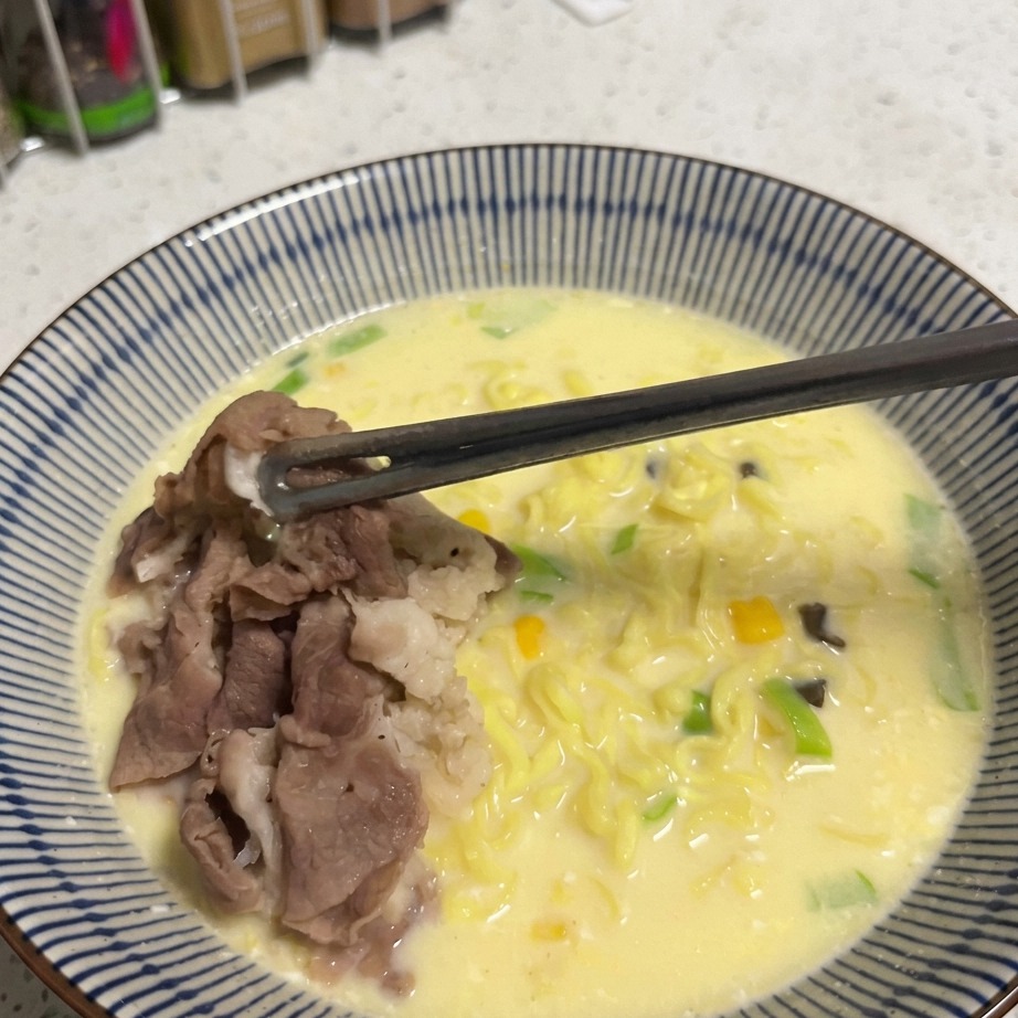 라면 한 그릇 위에 황금빛 스위트콘을 숟가락으로 뿌리는 모습.
