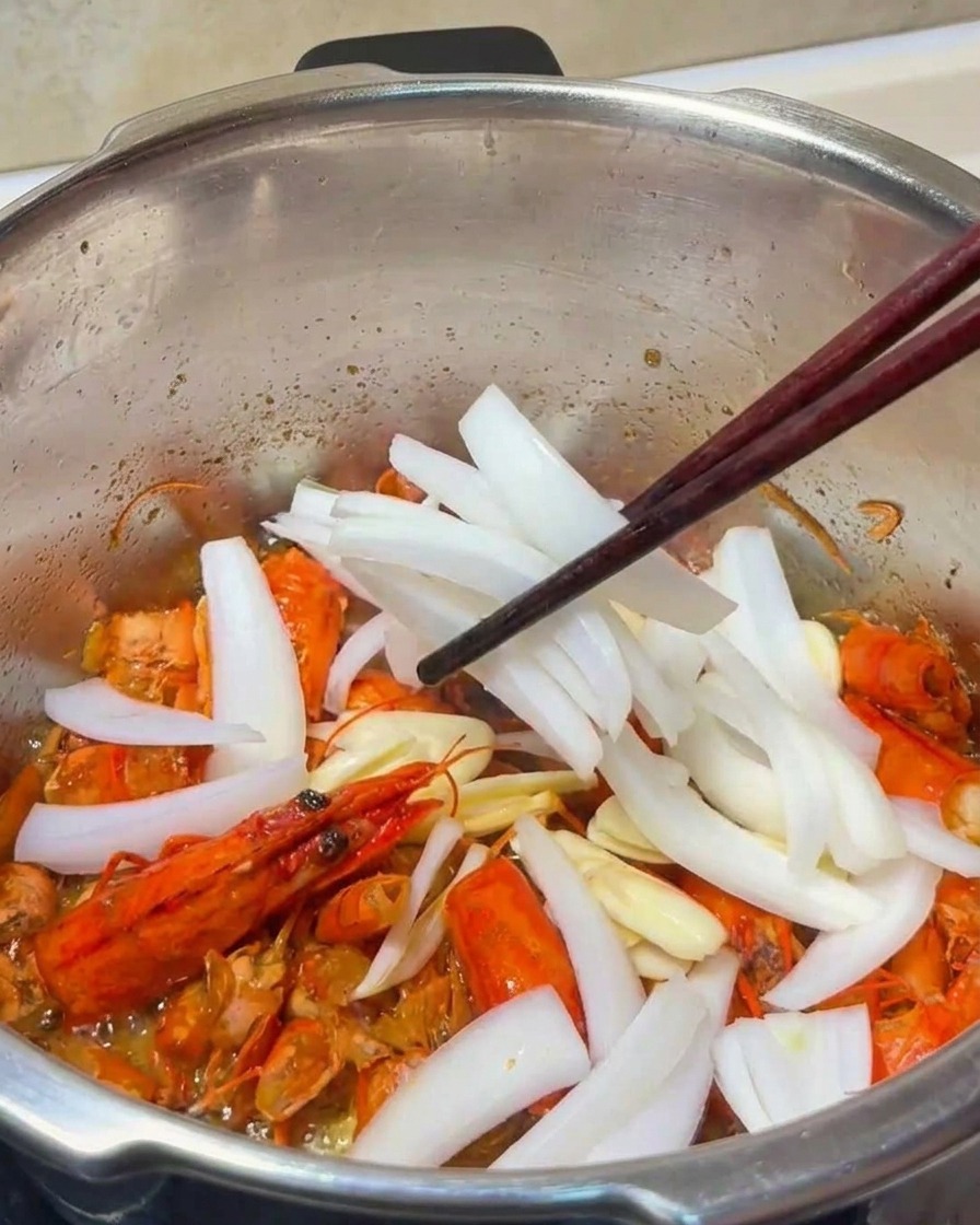 냄비에서 마늘과 양파가 새우 껍질과 섞이며 노릇하게 볶아지는 모습.