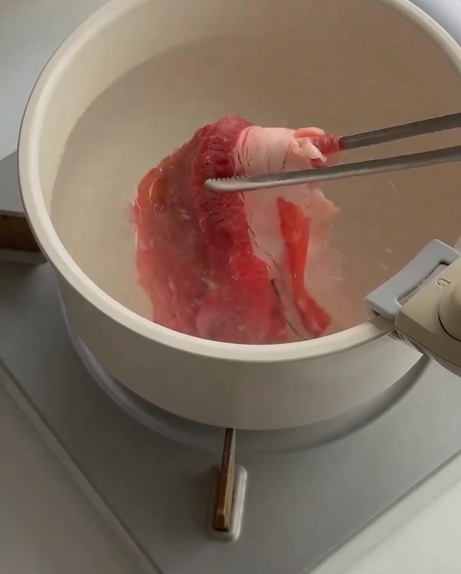 집게를 사용하여 끓는 물에 얇게 썬 소고기를 넣는 모습.