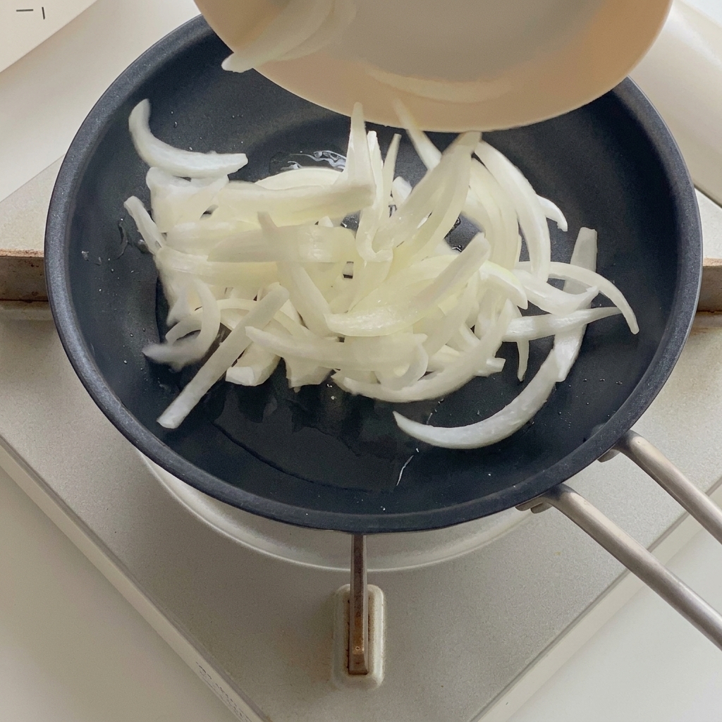 기름을 두른 팬에서 양파가 투명하게 볶아지는 모습.