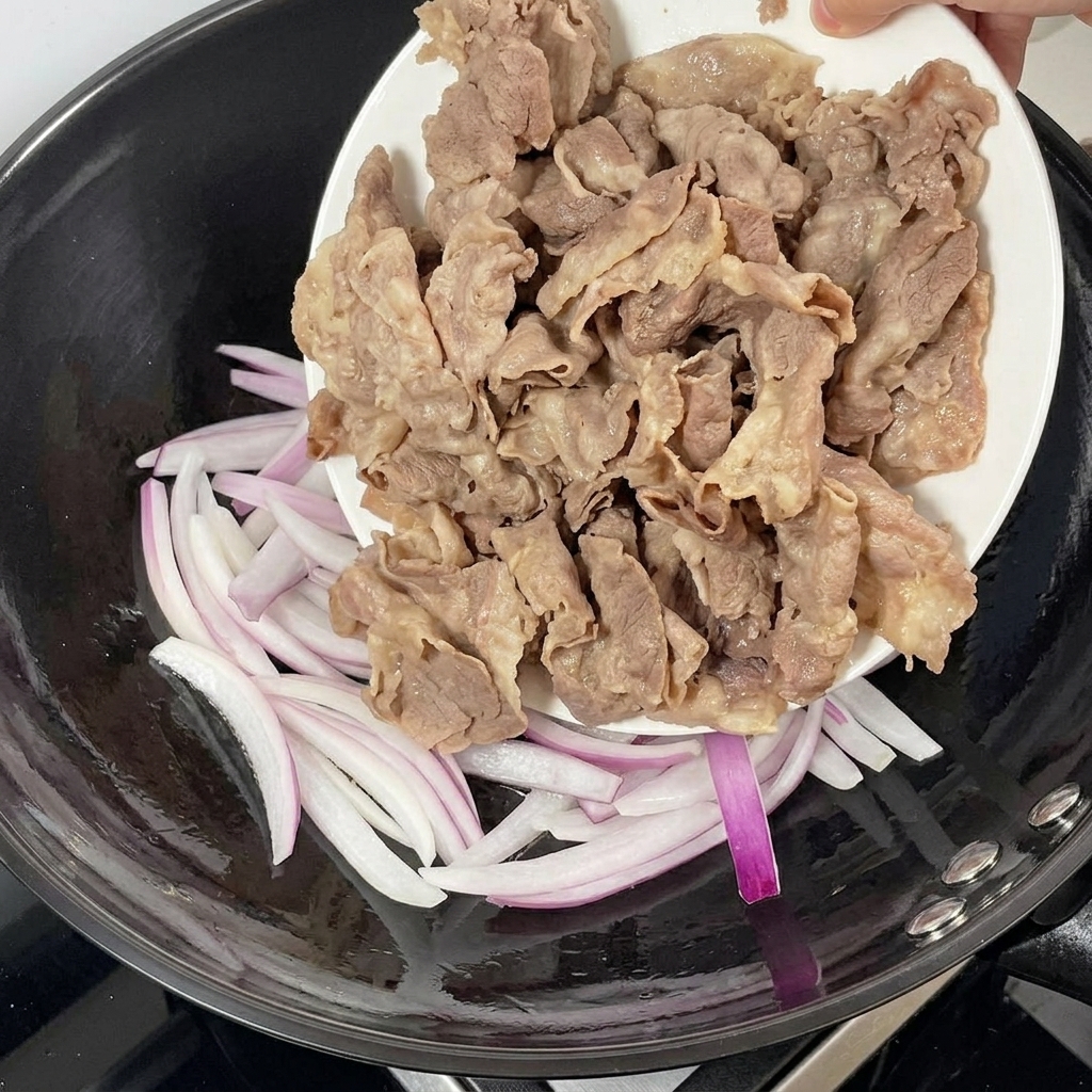 볶은 적양파가 담긴 팬에 데친 소고기를 넣는 모습.