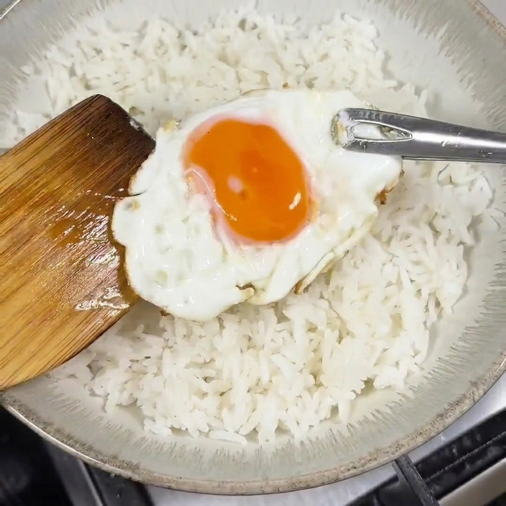 흰 쌀밥 위에 달걀프라이를 올리는 모습.