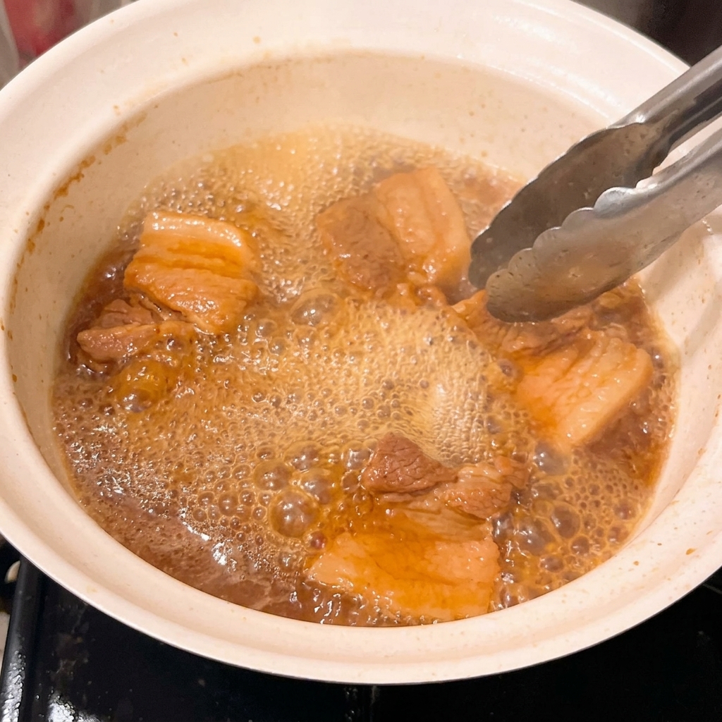 걸쭉하게 끓어오르는 미소 소스에 졸여지고 있는 부드러운 돼지고기.