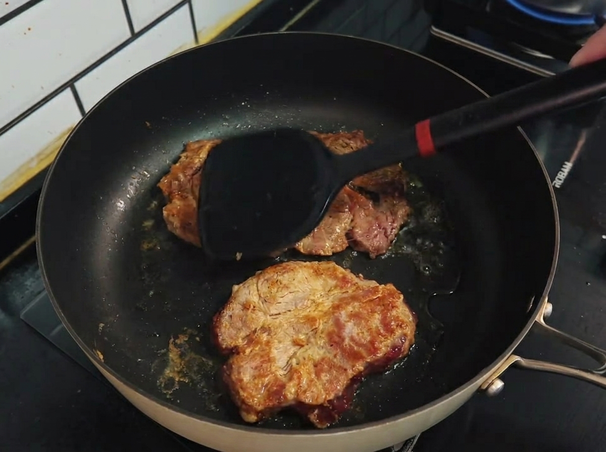 뒤집개로 코팅 팬 위에서 갈색으로 구워지는 돼지고기를 뒤집는 모습.