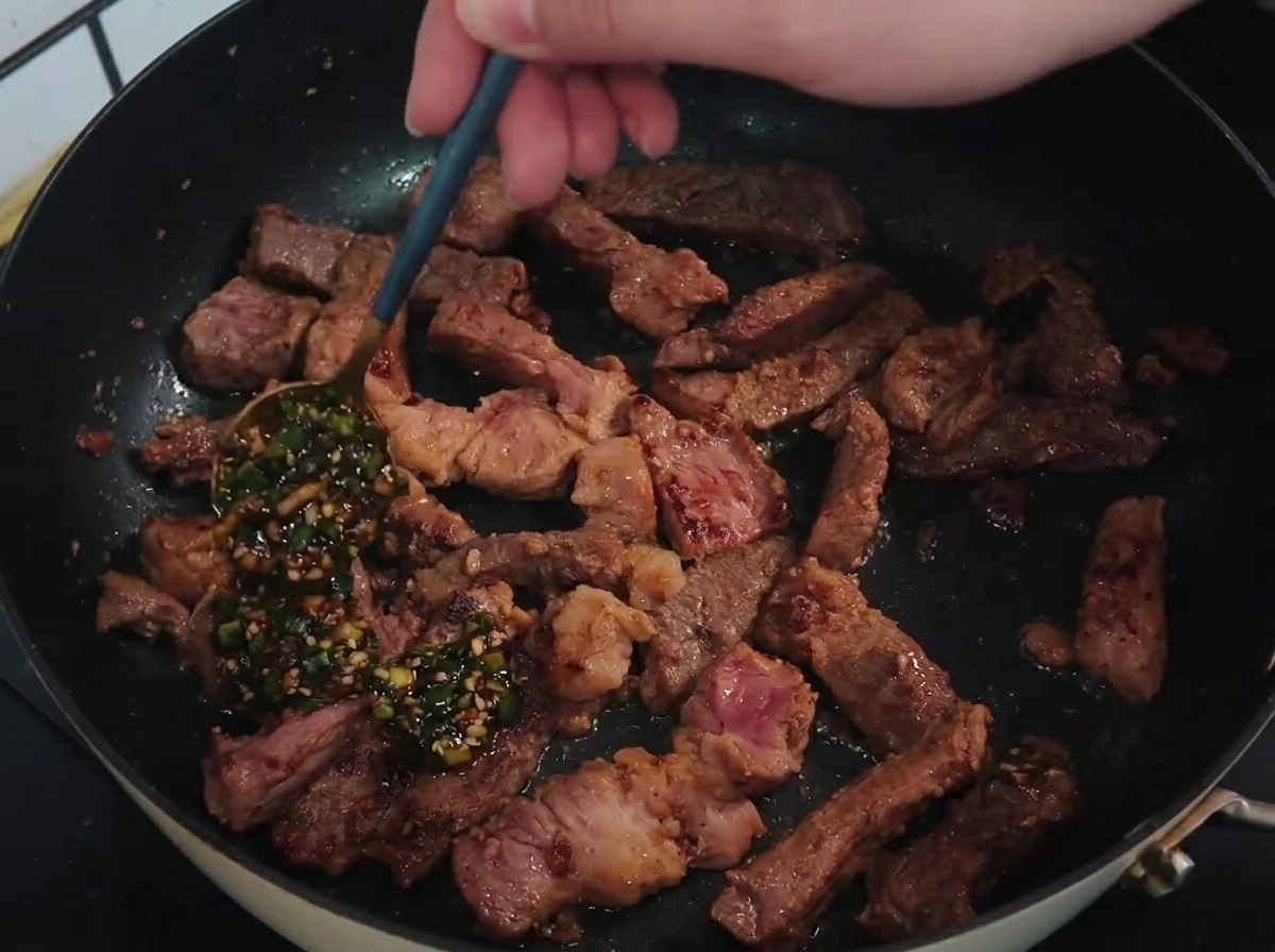 팬에 구워진 돼지고기 스트립 위에 준비한 쪽파 소스를 숟가락으로 뿌리는 모습.