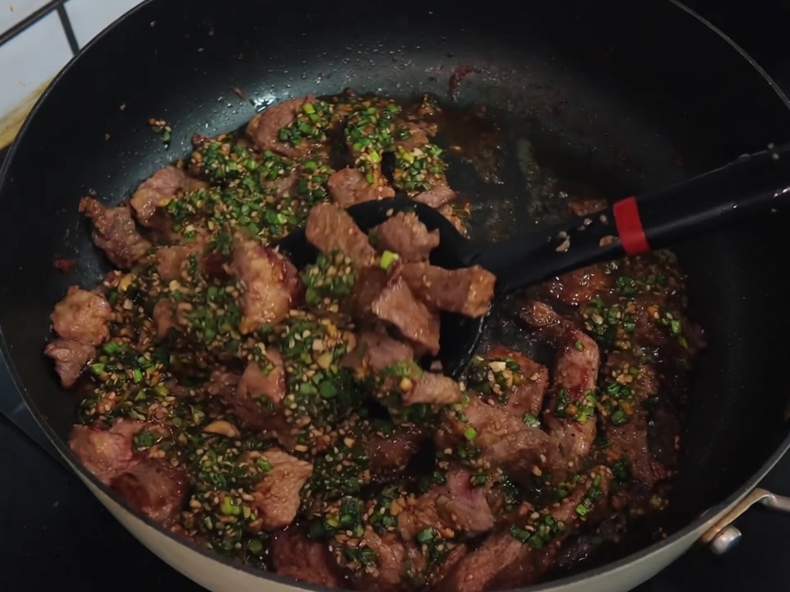 검은색 뒤집개로 소스와 고기를 가볍게 버무리며 볶는 모습.