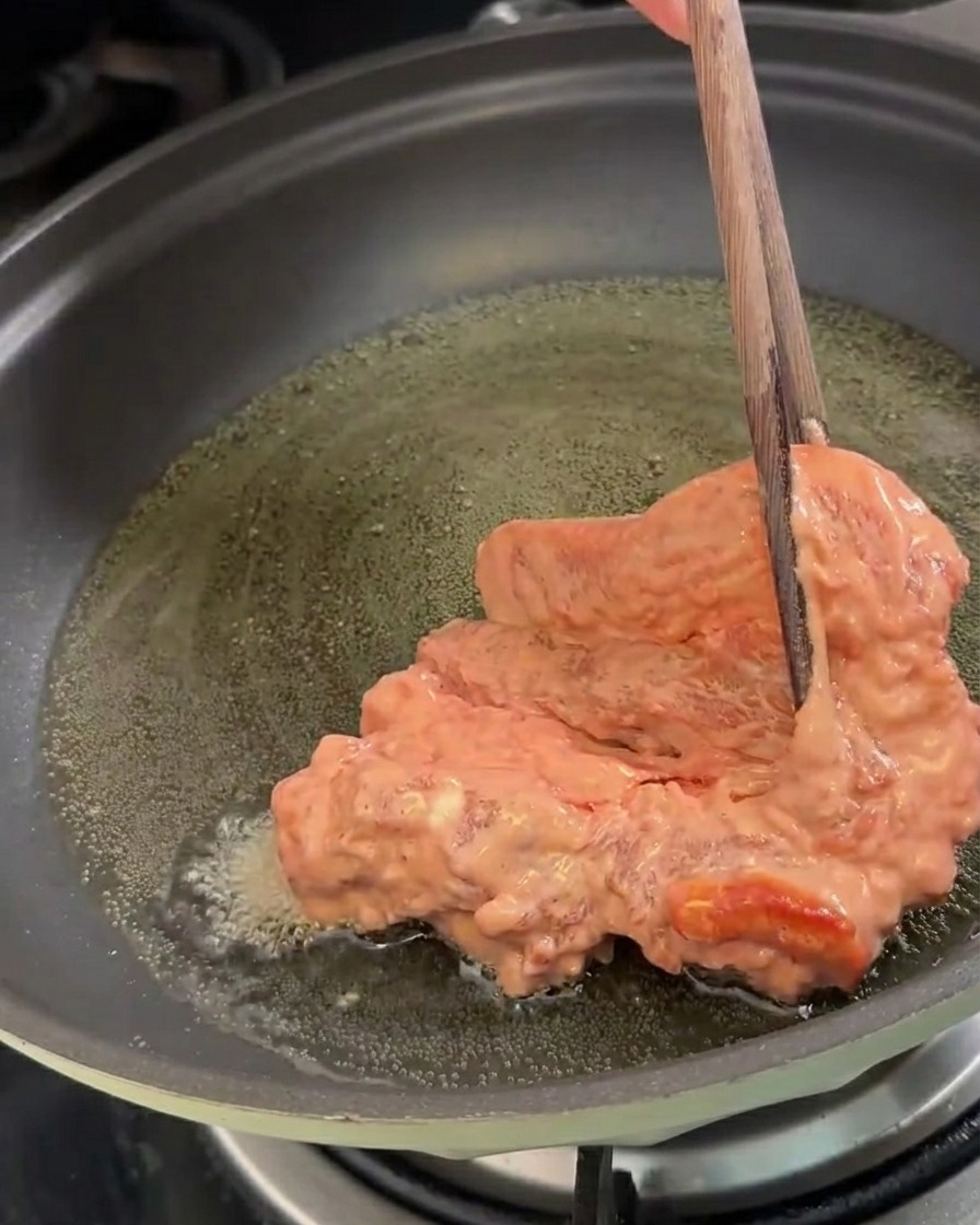 달궈진 기름에 전분을 입힌 삼겹살 조각을 조심스럽게 넣는 모습.