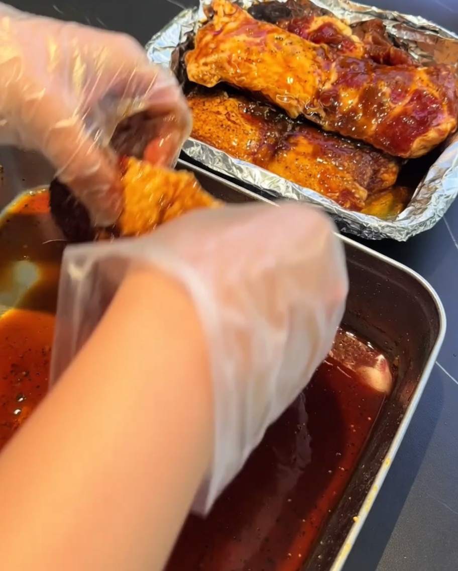 장갑을 낀 손으로 양념된 돼지갈비를 알루미늄 호일이 깔린 찜통에 옮겨 담는 모습.
