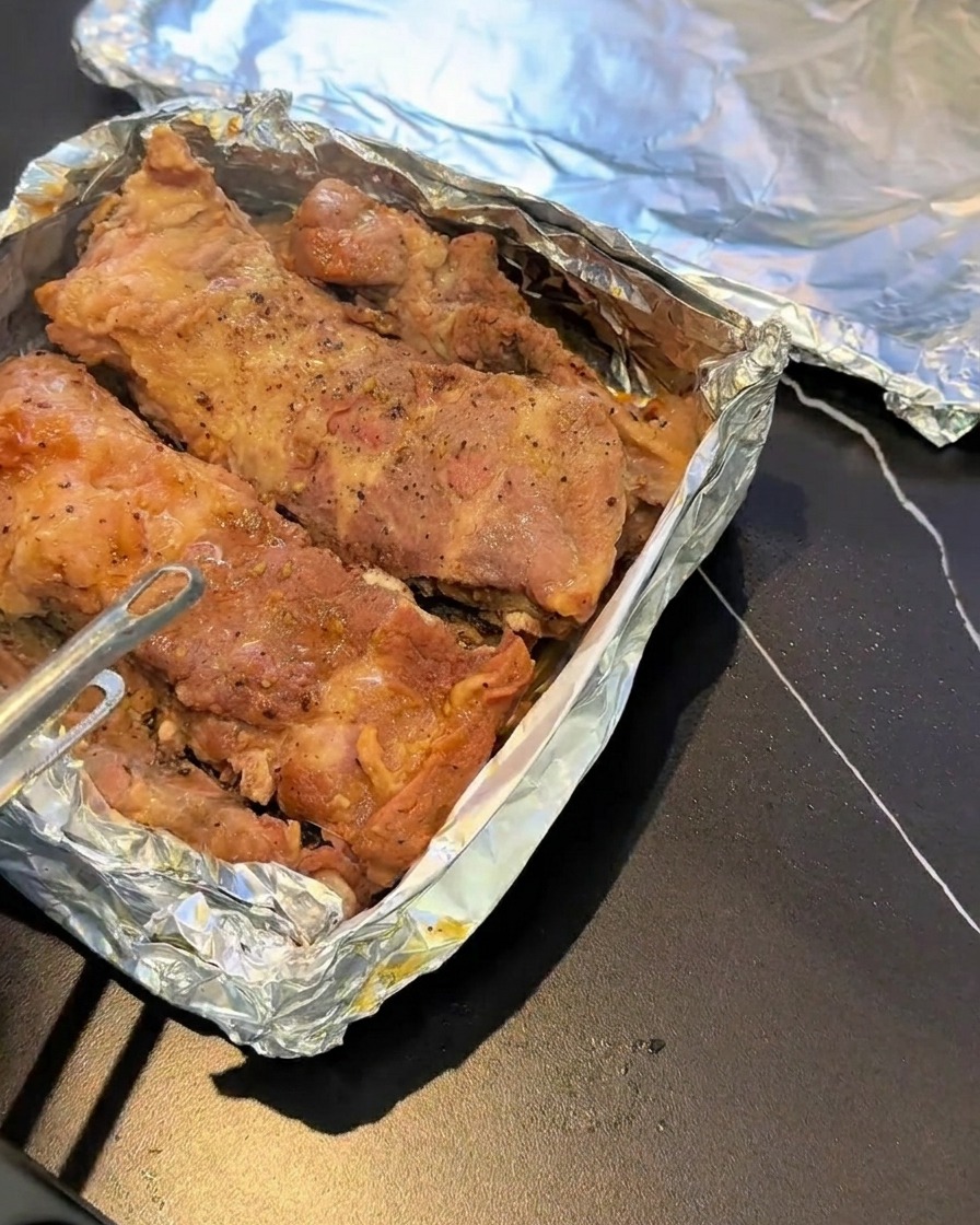 알루미늄 호일이 깔린 베이킹 시트 위에 놓인 찐 돼지갈비, 흑후추로 간이 된 모습.