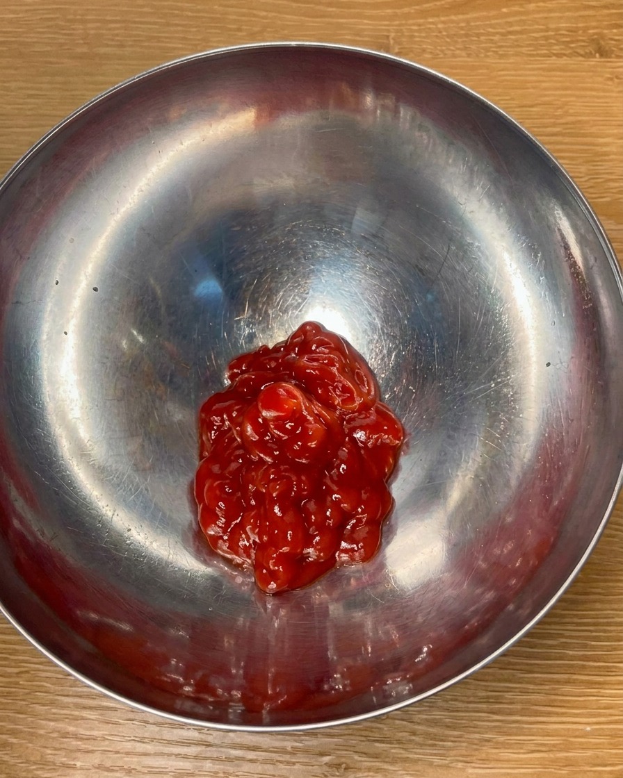 금속 볼에 토마토 케첩과 양념 재료를 넣고 섞어 소스를 만드는 모습.