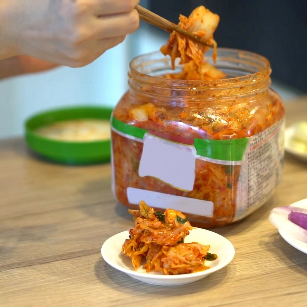 젓가락으로 용기에서 김치를 꺼내 접시에 담는 모습.