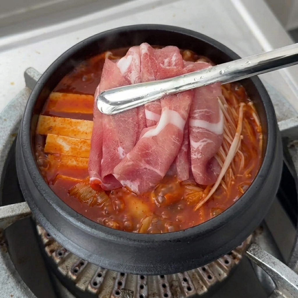 두부와 버섯 위에 생삼겹살 슬라이스를 올리는 모습.