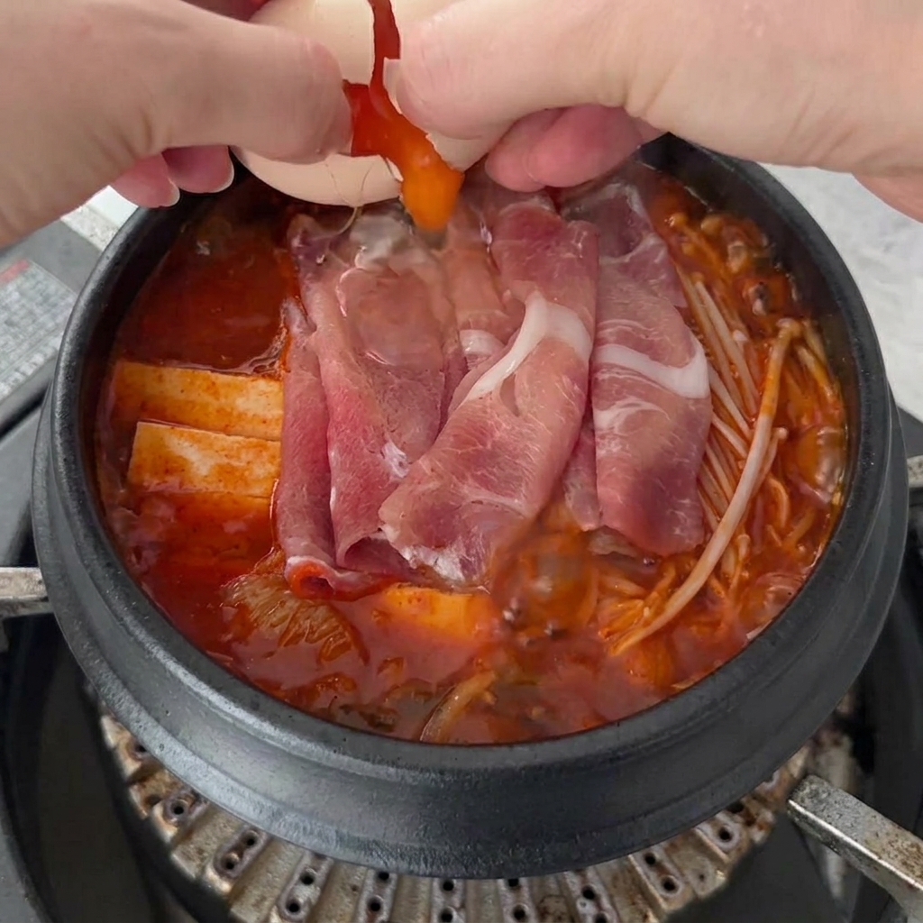 끓는 김치찌개 위에 계란 두 알을 깨 넣는 모습.