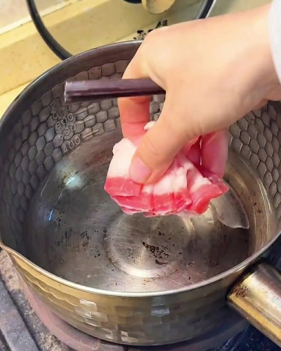 냄비에서 돼지고기 삼겹살을 볶아 기름이 배어 나오는 모습.