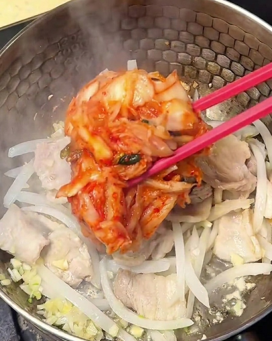 고기와 양파가 볶아진 냄비에 김치를 넣어 함께 볶는 모습.