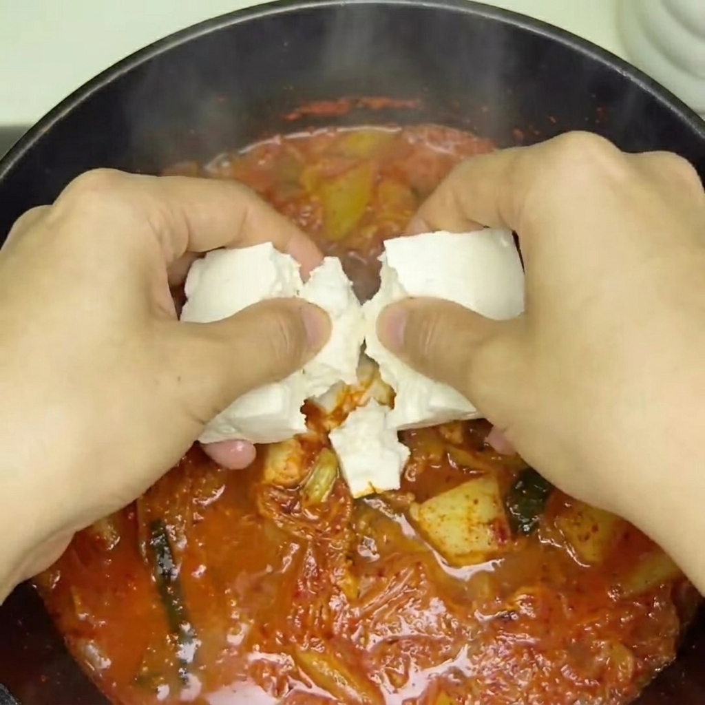 끓는 찌개 위에 두부와 팽이버섯을 올리는 모습.