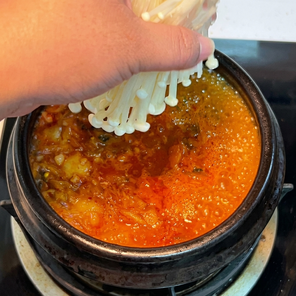 끓고 있는 김치찌개에 팽이버섯을 넣는 모습.
